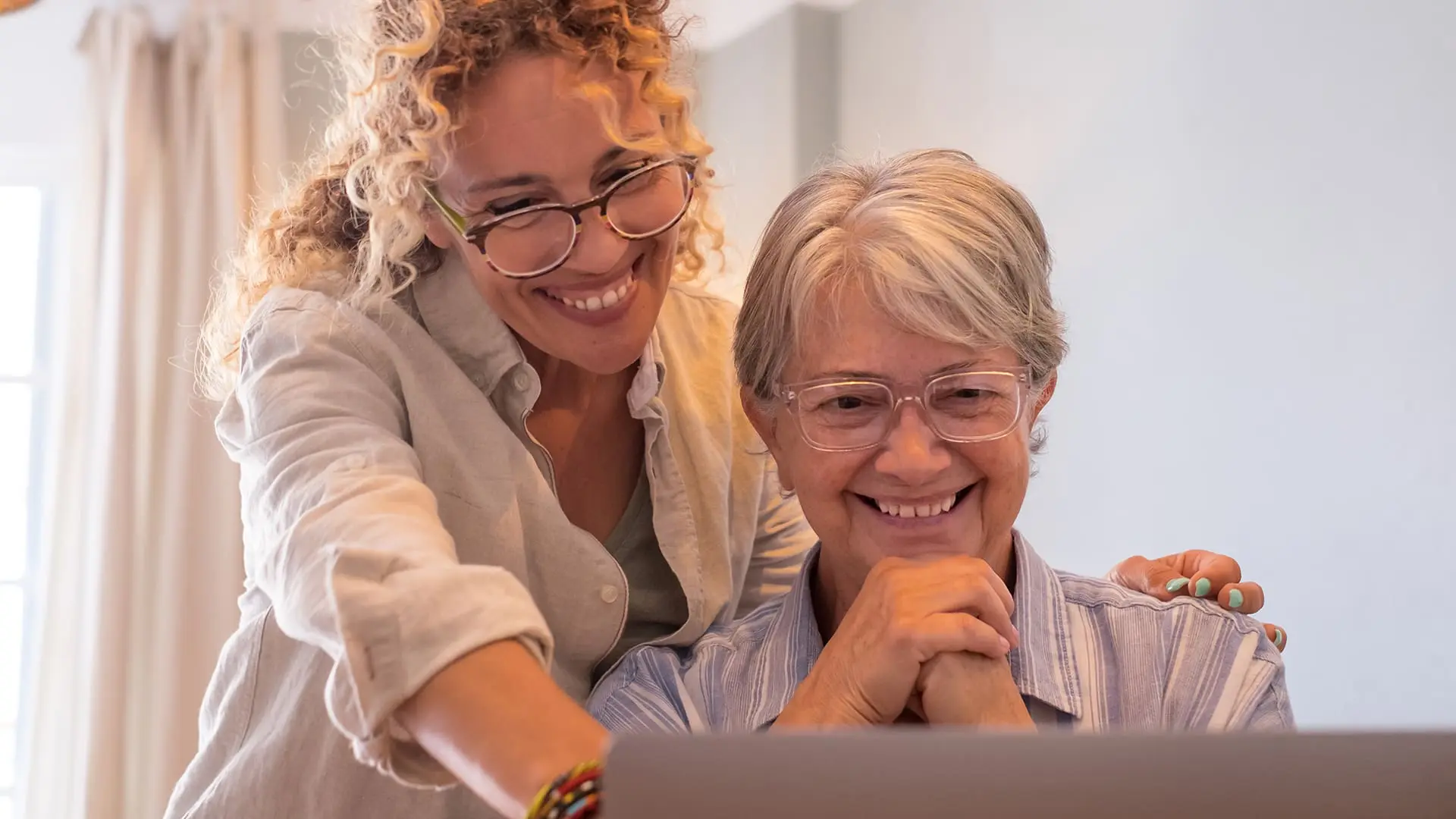 iStock-1316760408_1920x1080 senior woman and her adult daughter smiling and pointing at their laptop screen