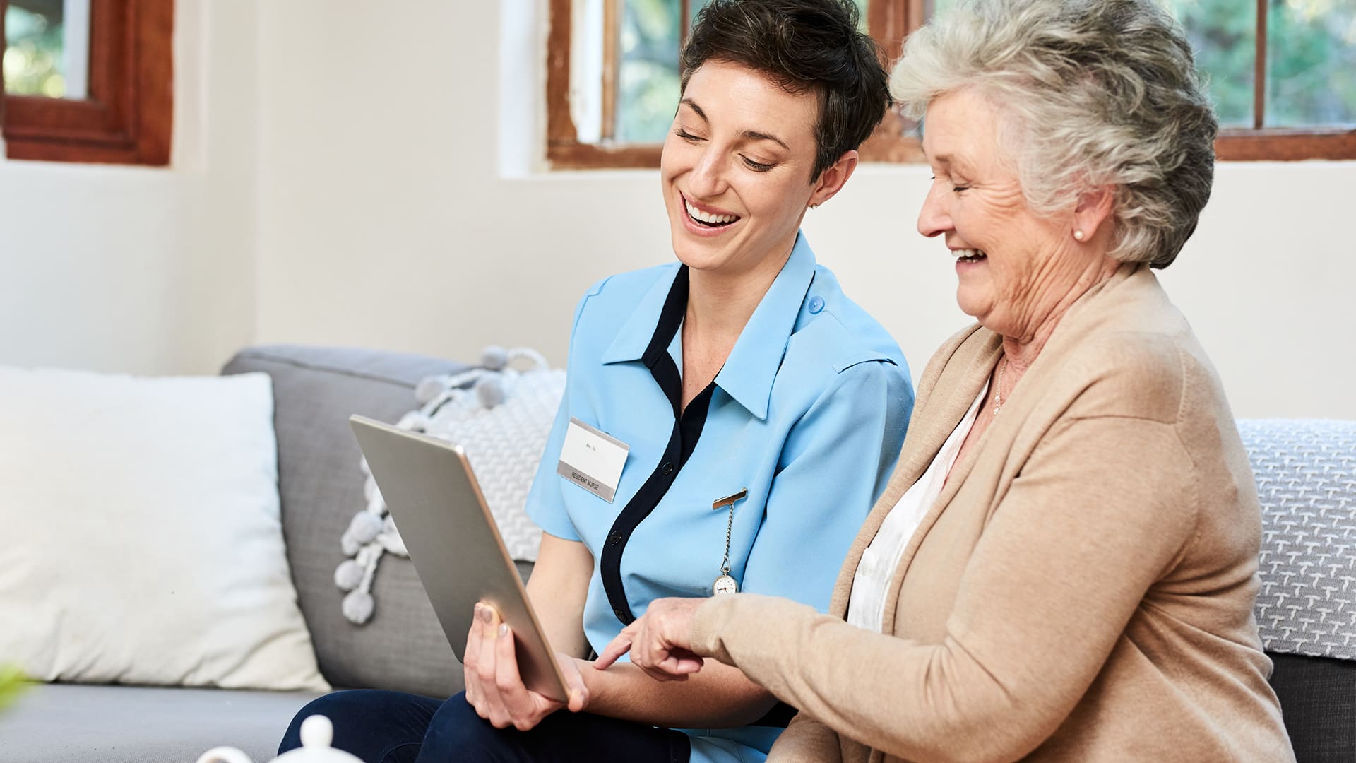 nurse caregiver helping senior woman video call with family on a tablet device