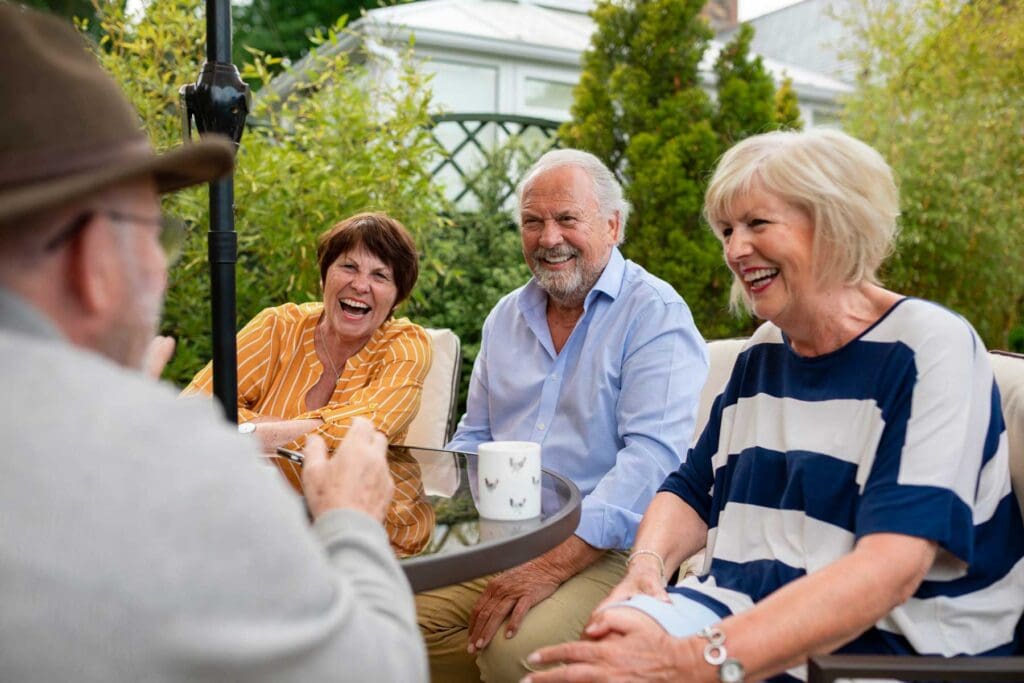 a group of senior friends laughing together while sitting around a table outside